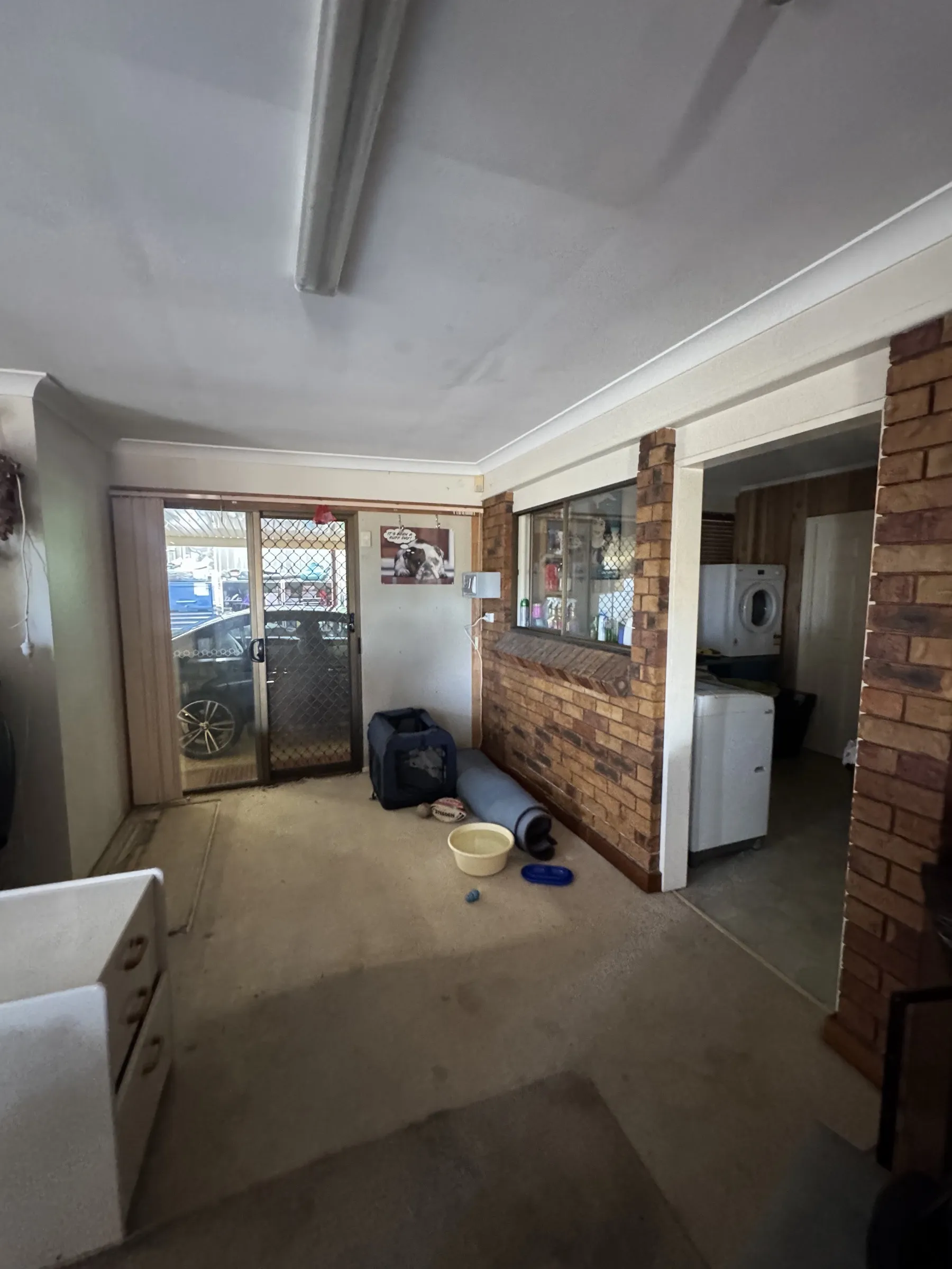 Before: garage interior showing cluttered storage, brick wall, and existing laundry appliances before the garage tidy and reorganisation work