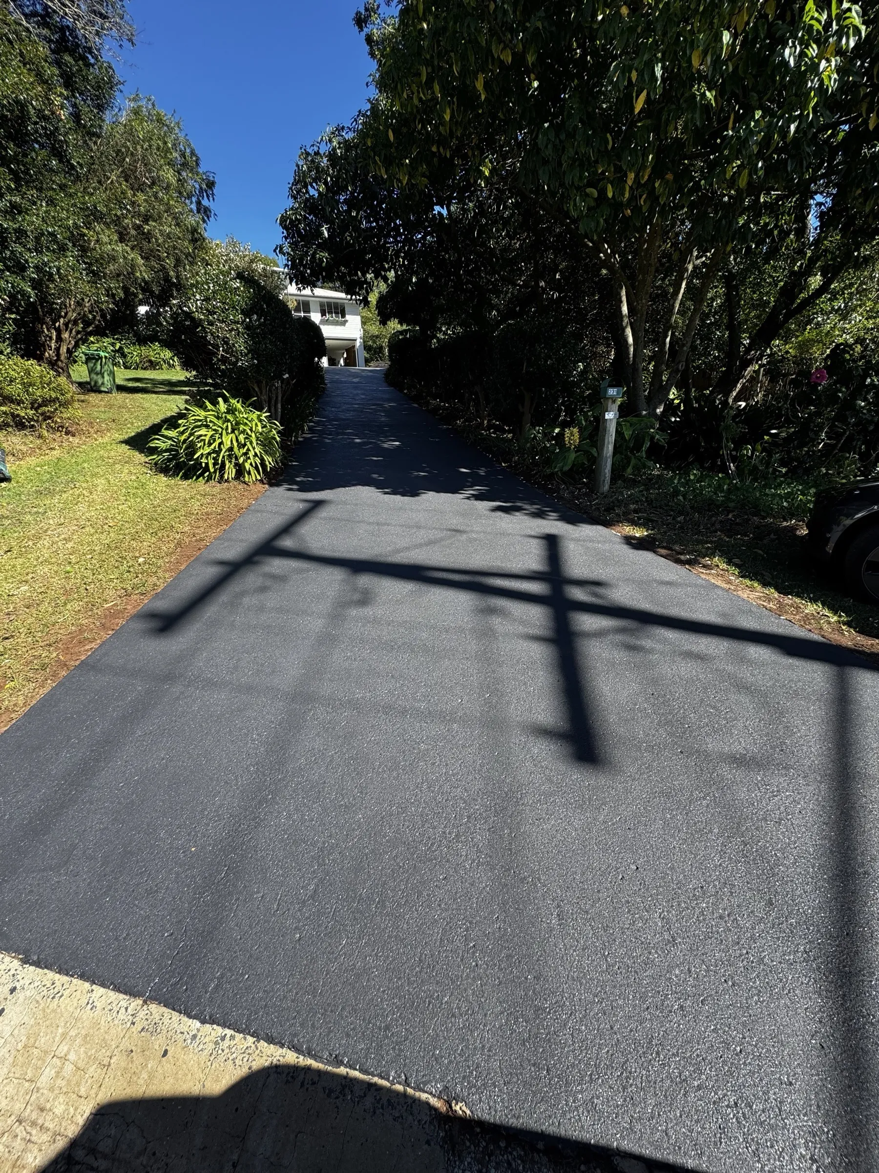 Freshly resealed dark charcoal driveway edged by mature trees, showing the clean finish achieved after resurfacing on a regional Toowoomba property