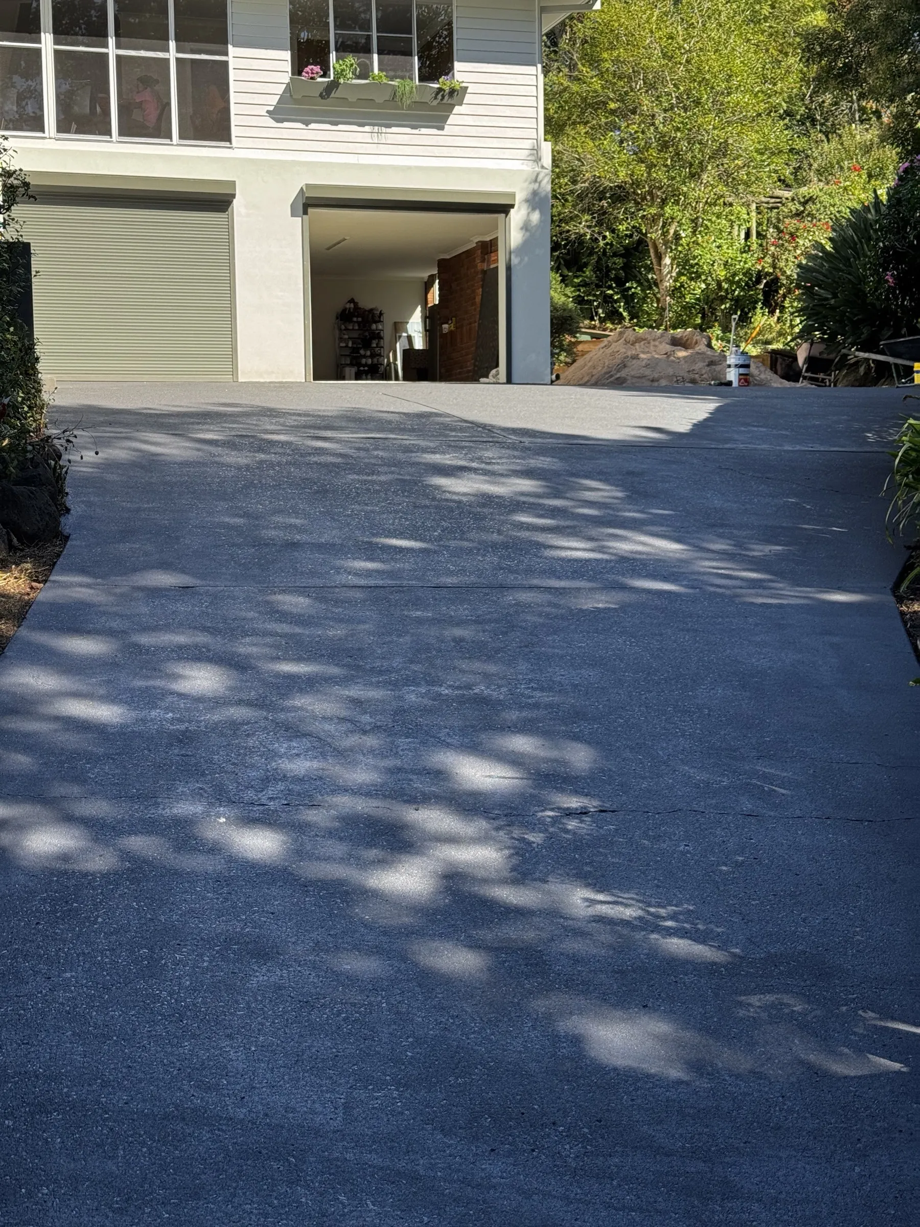 Resealed dark charcoal driveway beside a weatherboard home exterior, with afternoon light showing the uniform finish of the completed work