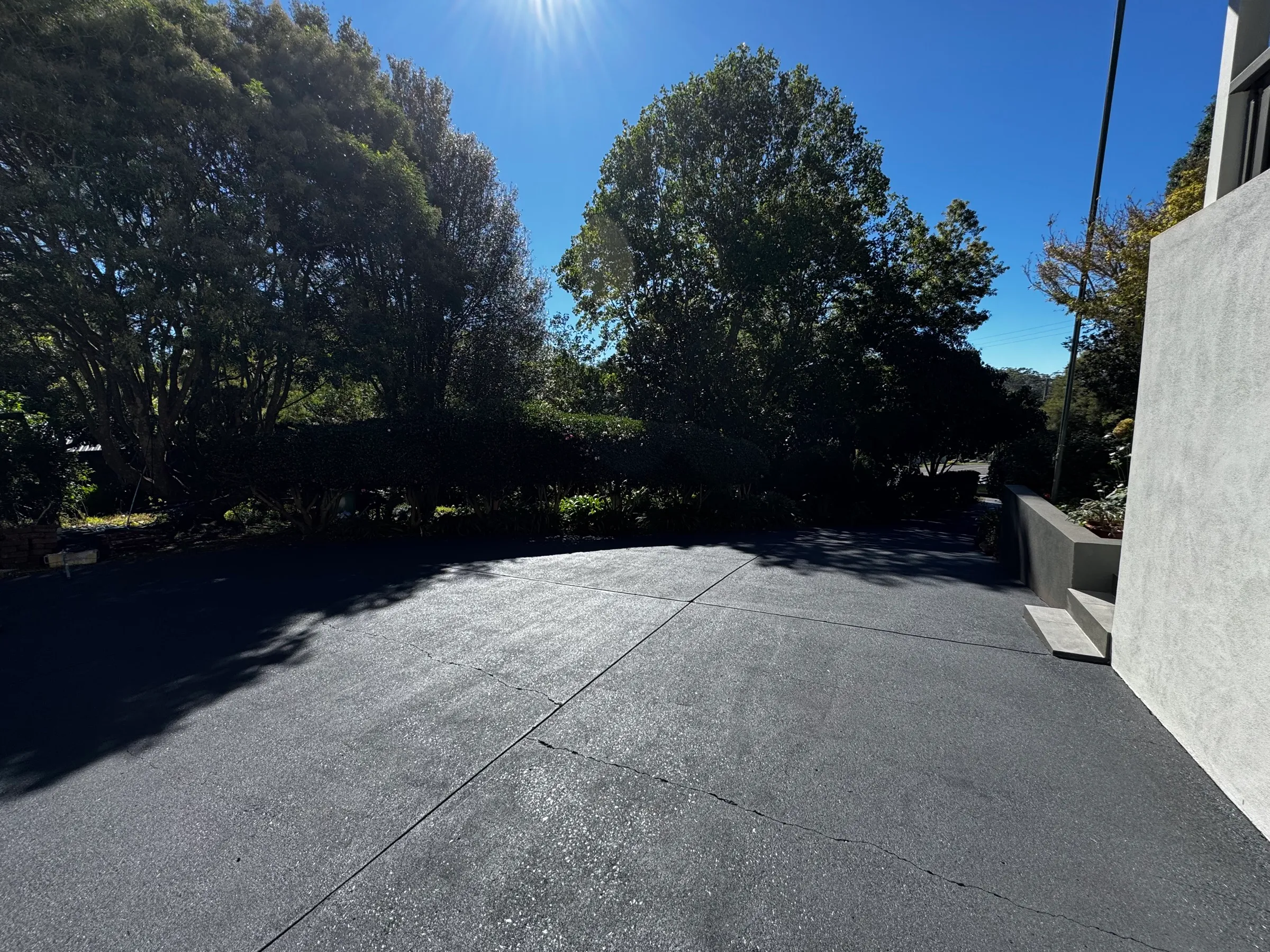 Wide freshly resealed dark driveway curving beside a modern rendered home, with gum trees and bright Queensland sunlight — Toowoomba region