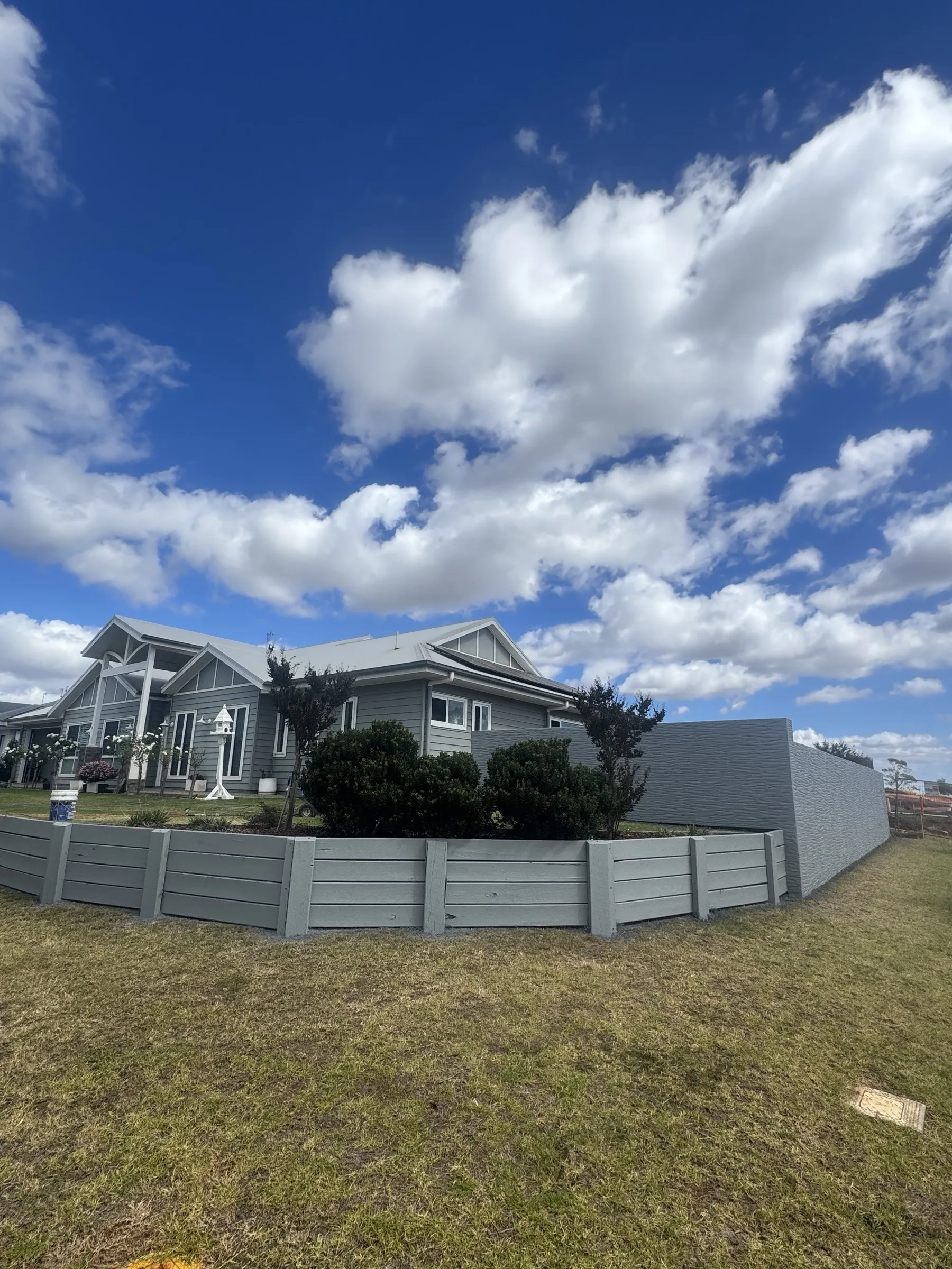 A completed custom grey panel fence running along the front of a residential property in the Darling Downs, with a house and blue Queensland sky behind