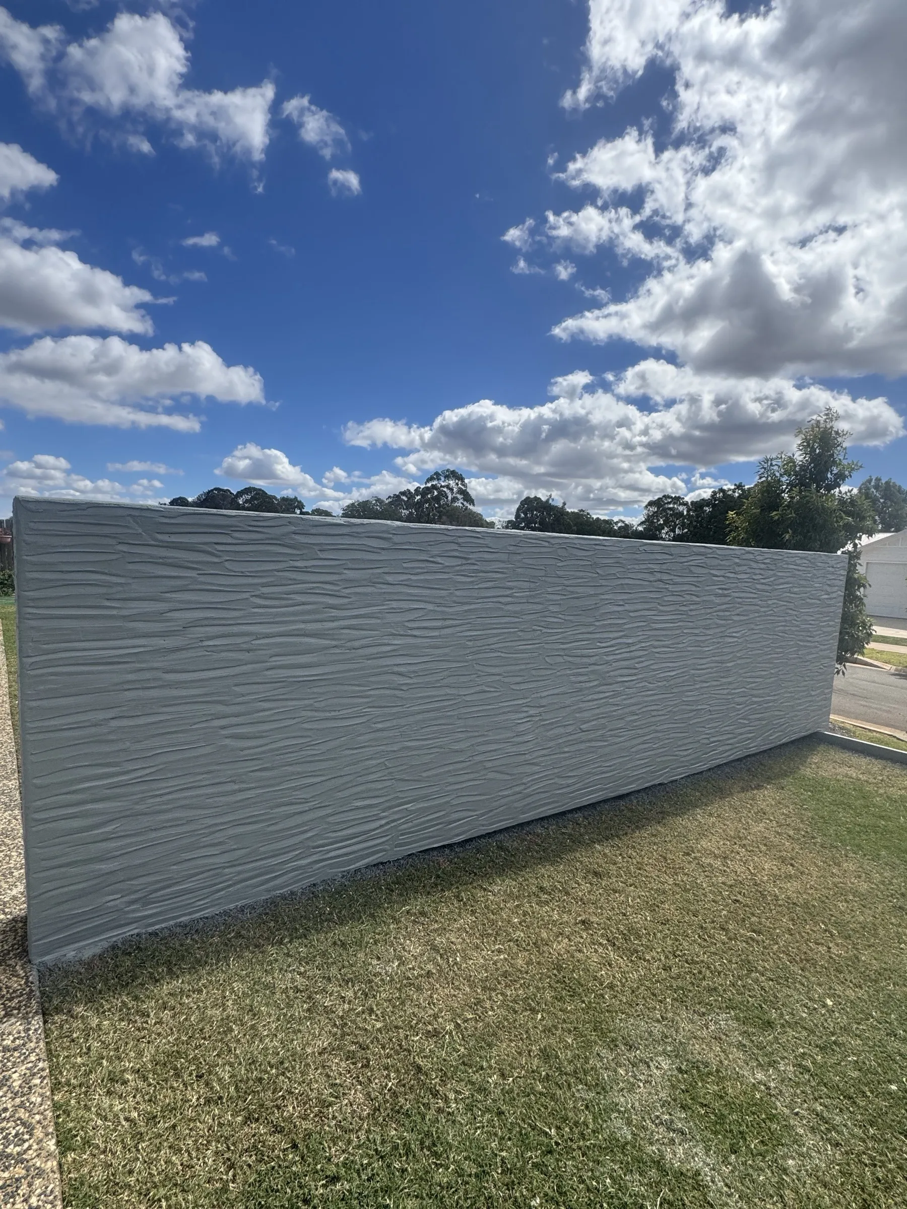 Full-length run of a custom grey panel fence against an open blue sky with gum trees, showing the scale and clean line of the finished install
