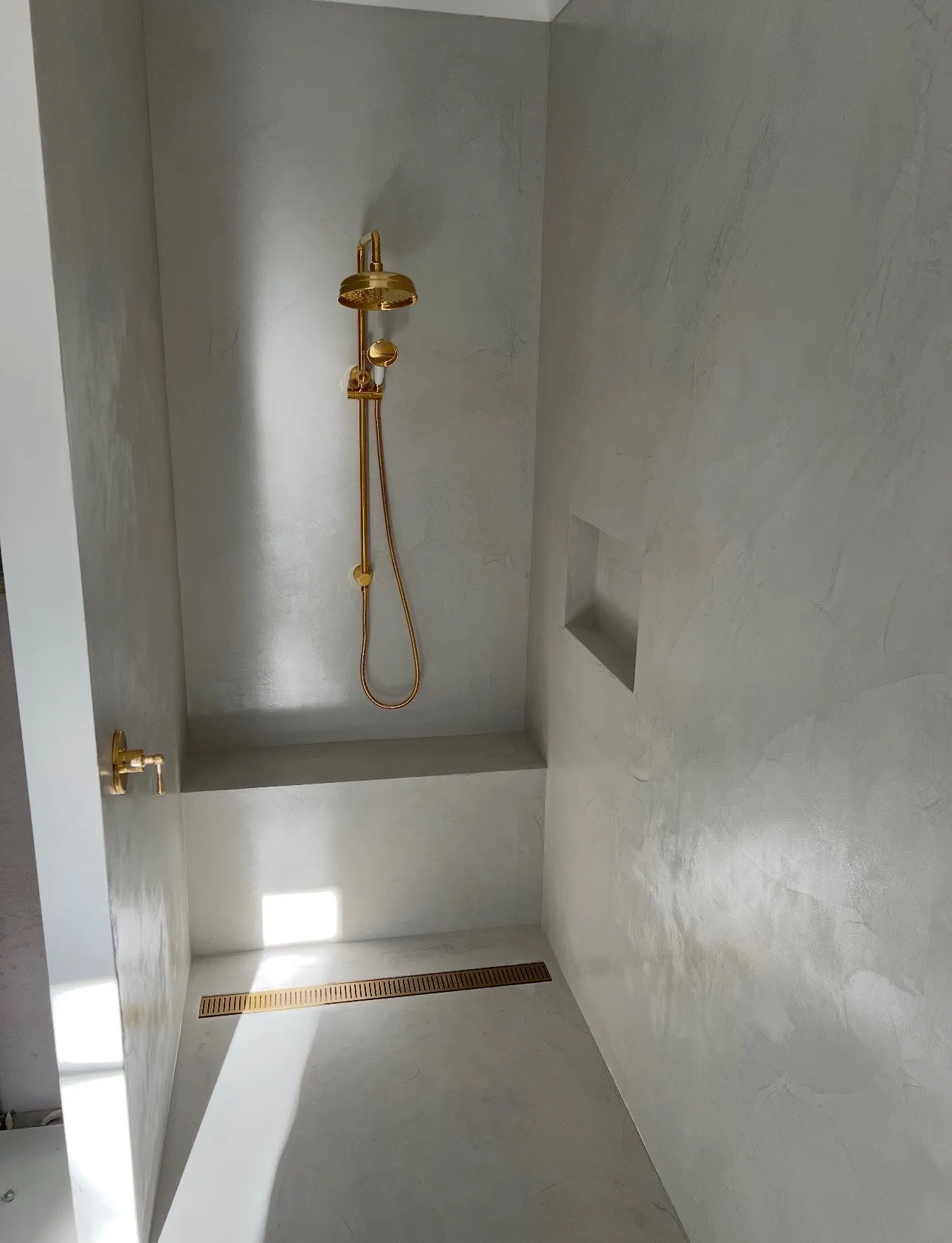 A finished bathroom with seamless polished micro cement walls and a brass shower fitting