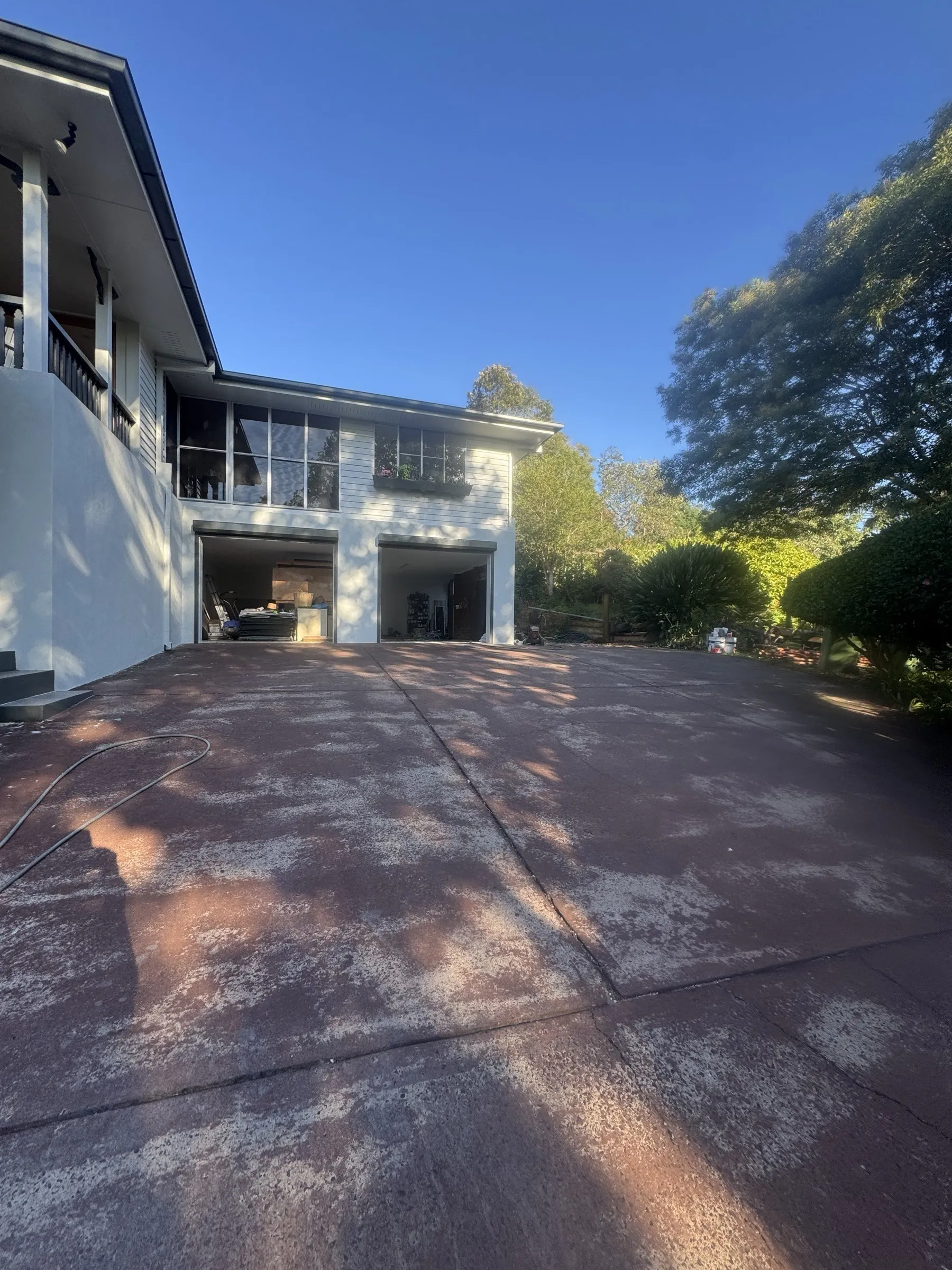 Wide concrete driveway in front of a large two-storey home, freshly resurfaced and cleaned, showing the scale of the exterior work completed