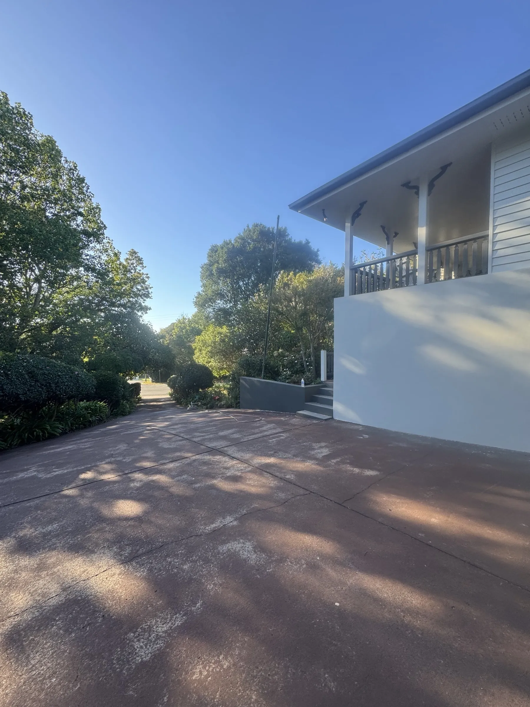 Side view of a freshly painted white rendered home exterior with a newly resurfaced red driveway and mature garden, regional Toowoomba