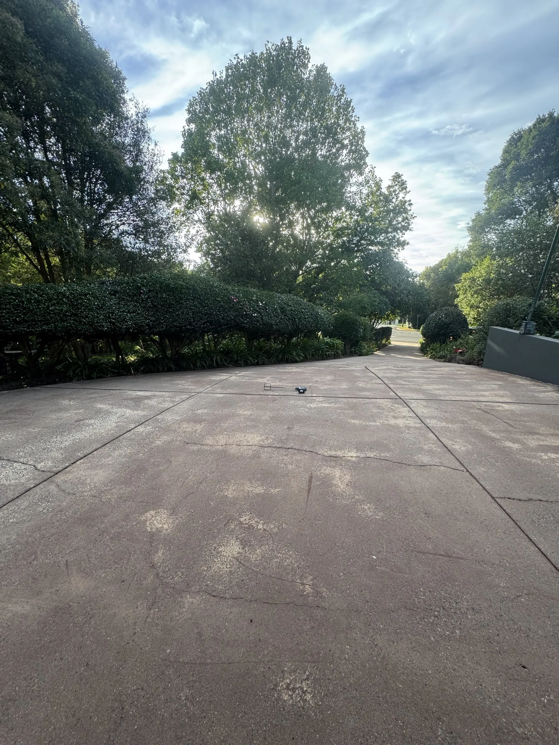 Driveway approach to a residential property with pressure-washed concrete visible and established garden beds, ready for next phase of exterior work