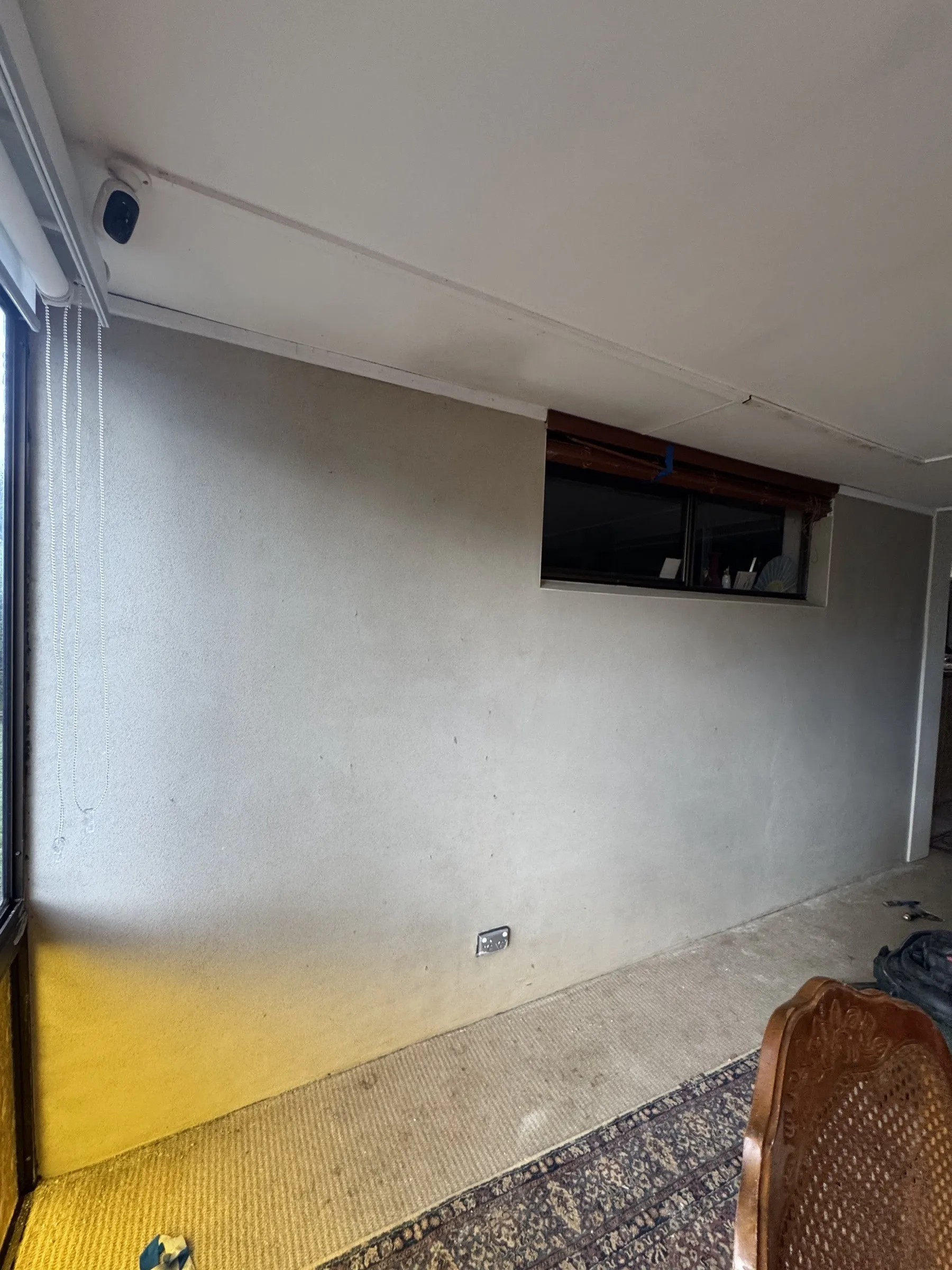 Before: freshly skimmed interior wall ready for painting, with old floor coverings still in place and existing window and furnishings visible