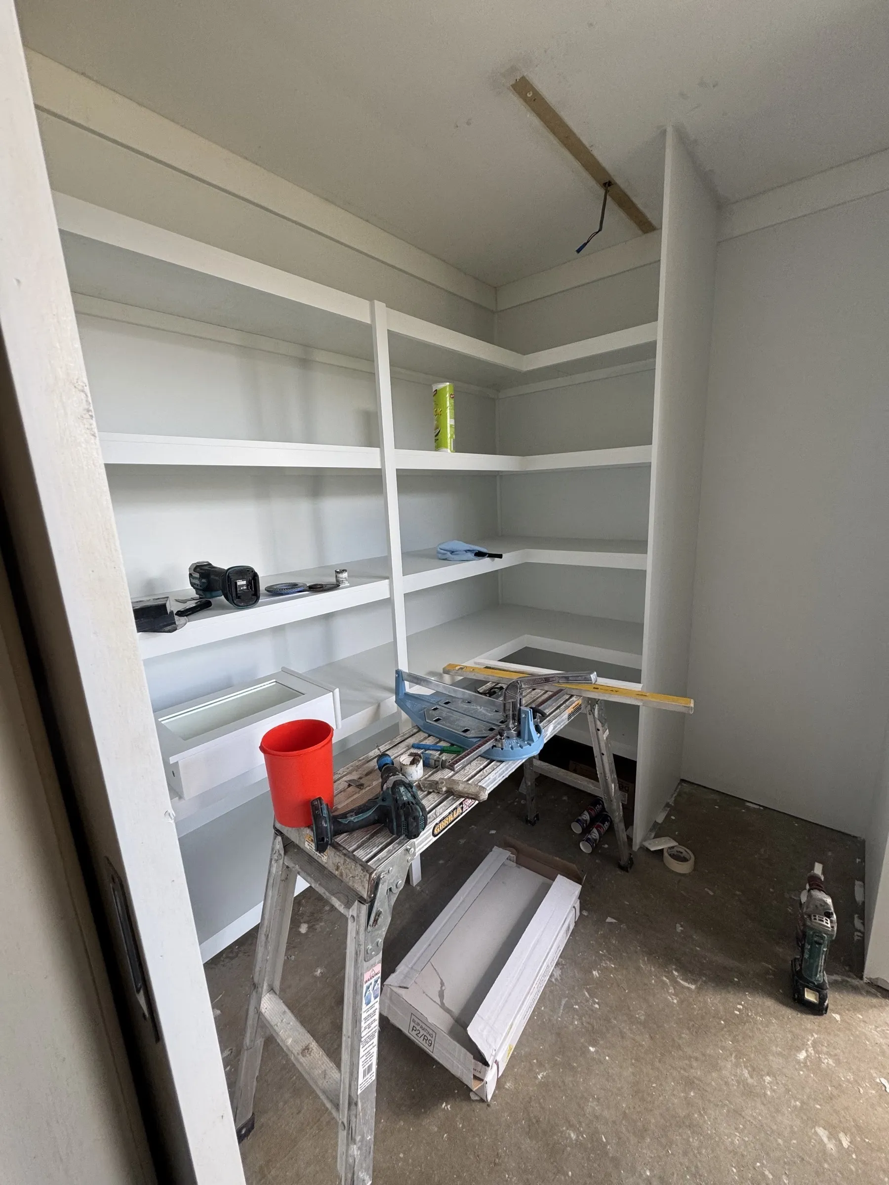 Built-in shelving and cabinetry under construction inside a domestic property, showing the carpentry framing and white-painted shelves mid-install