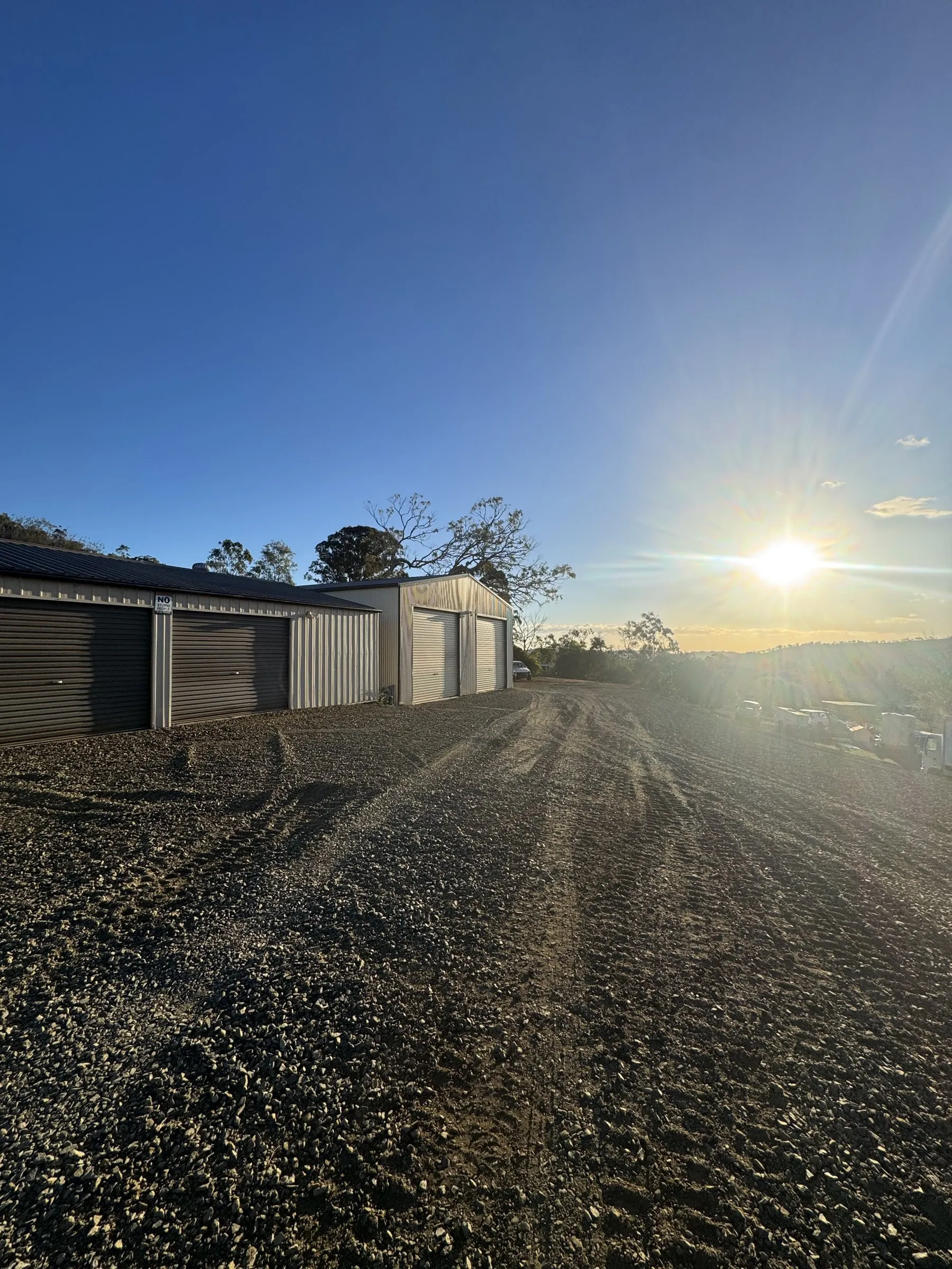 A large cleared and graded rural site at sunset with farm sheds along one edge, showing the scale of an earthworks and yard-clearing project in the Southern Downs
